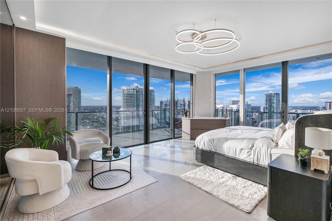 Floor-to-ceiling windows, wrap-around balcony with glass railings, large-format tile flooring, recessed cove lighting, and contemporary circular multi-tier chandelier