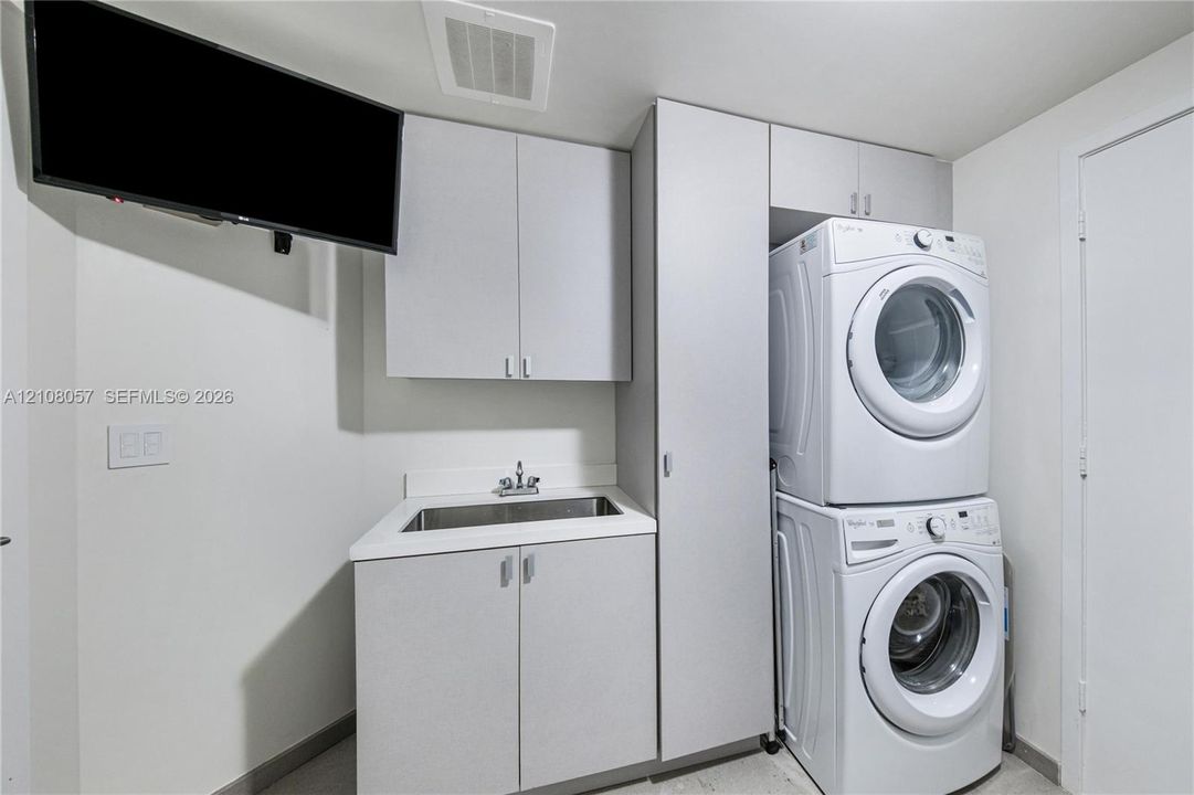 Laundry room featuring cabinetry with light-colored laminate finishes, a rectangular drop-in sink, and a vertical stacked laundry center