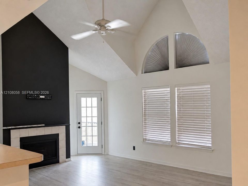 Vaulted ceilings featuring a ceiling fan, tiled fireplace with a monochromatic accent wall, arched windows, and wood-finish flooring