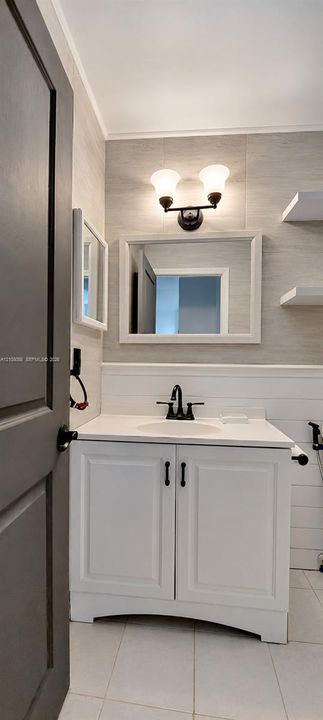 White vanity with an integrated basin, white shiplap wainscoting, matte black faucet, wall-mounted light fixture, and floating shelving