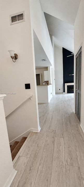 Vaulted ceilings with architectural height, wood-finish flooring, floor-to-ceiling fireplace surround, and wall-mounted sconce lighting