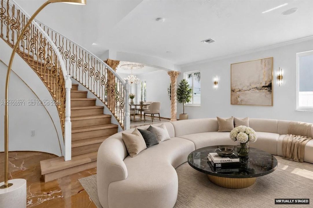 Curved staircase with wood-finish treads and ornate metal railings, stone flooring, and decorative column accents