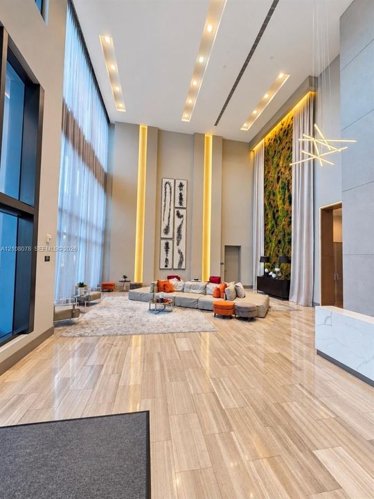 Double-height ceiling featuring recessed linear lighting, floor-to-ceiling windows, polished stone-finish flooring, and a decorative interior living wall