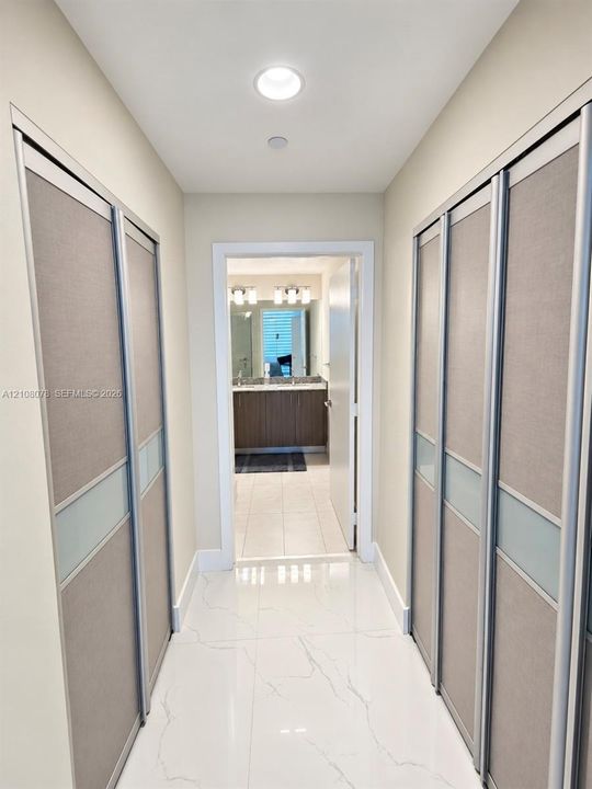 Hallway featuring large-format tile flooring and dual wall-to-wall closets with sliding panel doors, recessed ceiling lighting, and brushed metal trim