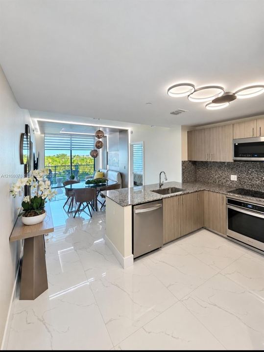 Kitchen featuring light wood-finish cabinetry, stone countertops, stainless steel appliances, and large-format porcelain tile flooring