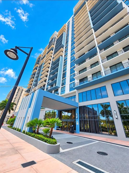 High-rise architecture featuring a covered porte-cochère, multi-level private balconies, floor-to-ceiling glass windows, and concrete exterior facade with integrated landscaping