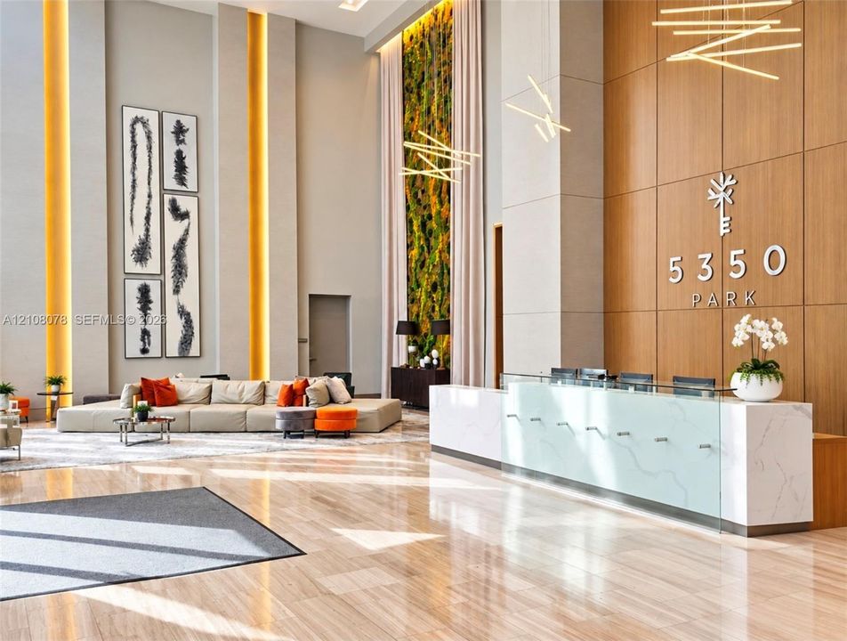 Double-height lobby featuring a polished stone floor, floor-to-ceiling wood-panel accent wall, custom reception desk with a stone countertop, vertical accent lighting, and a living plant feature wall