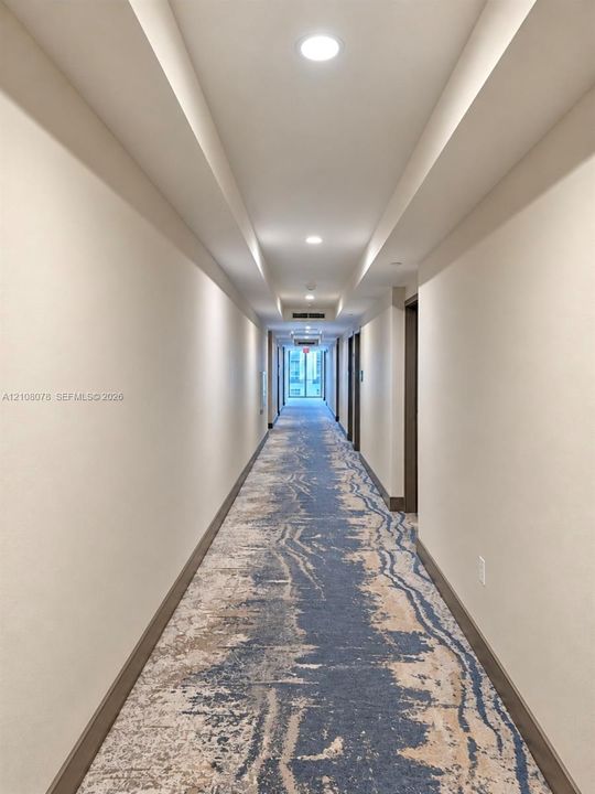 Hallway featuring neutral wall finishes, recessed ceiling lighting, tray ceiling detail, and patterned carpeting