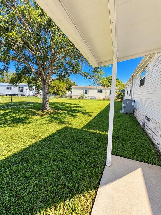 Covered concrete patio, expansive lawn, mature shade tree, perimeter wire fencing, and white horizontal siding