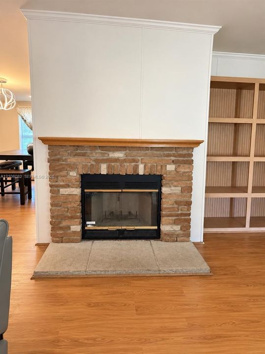 Fireplace featuring a masonry surround, wood-finish mantel, and stone hearth, accompanied by built-in wood shelving and wood-finish flooring
