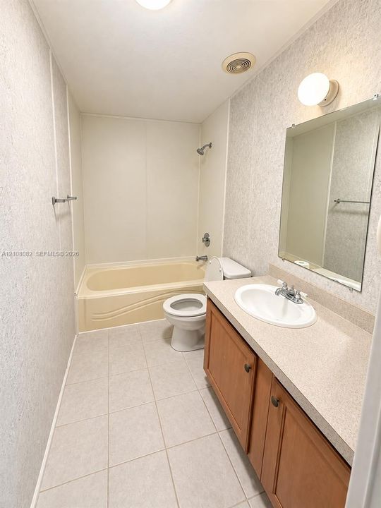 Bathroom featuring wood-finish vanity cabinetry, integrated countertop with oval basin, frameless wall-mounted mirror, and tile flooring