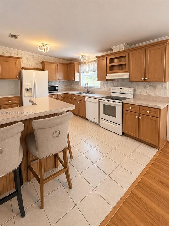 Kitchen featuring wood cabinetry, stone-texture laminate countertops, ceramic tile flooring, and integrated white appliances