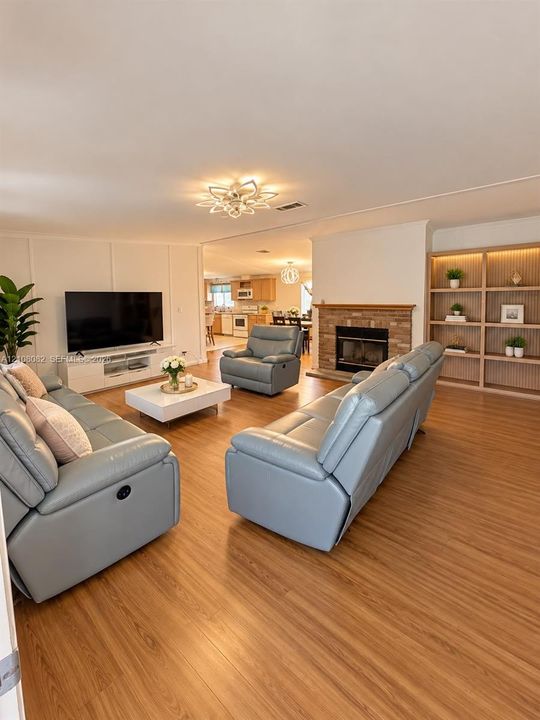 Living area featuring wood-finish flooring, a brick fireplace with a wood mantel, floor-to-ceiling built-in shelving, wall paneling, and a geometric flush-mount light fixture