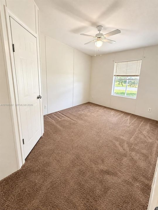 Interior room featuring neutral carpeting, a white paneled door, a single-hung window with horizontal blinds, and a white ceiling fan with integrated lighting