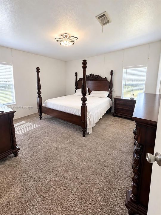 Neutral-toned carpeted flooring, decorative multi-bulb flush mount ceiling light, and dual windows equipped with horizontal blinds