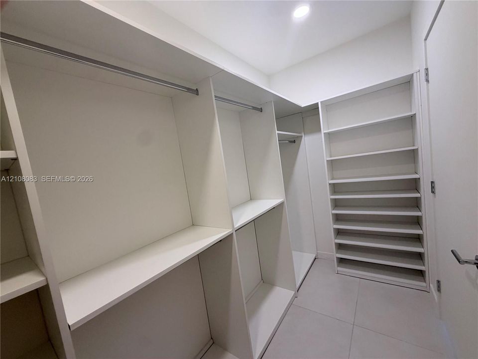 Walk-in closet featuring white built-in shelving, integrated hanging rods, and large-format tile flooring
