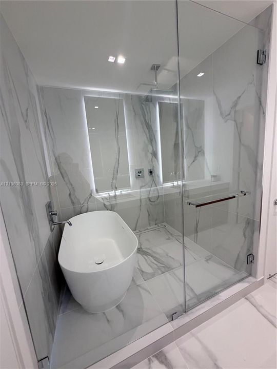 Wet room featuring floor-to-ceiling large-format stone-patterned tile, a freestanding oval soaking tub, and a frameless glass enclosure with a rainfall shower head