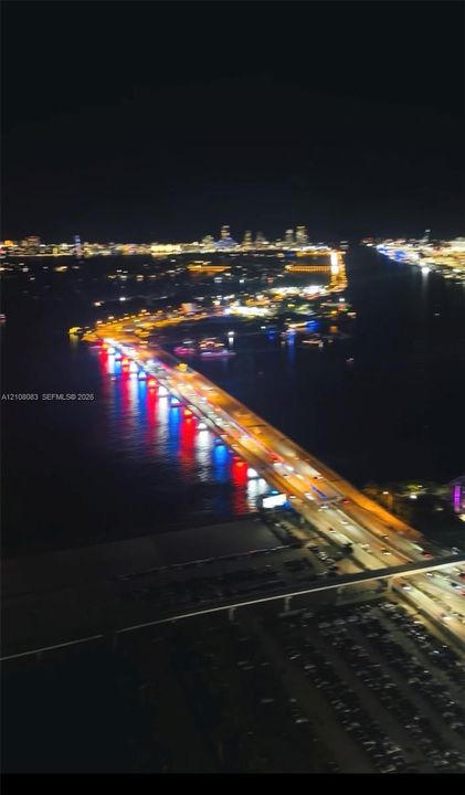 Aerial perspective featuring illuminated cityscape, expansive waterway, and bridge infrastructure