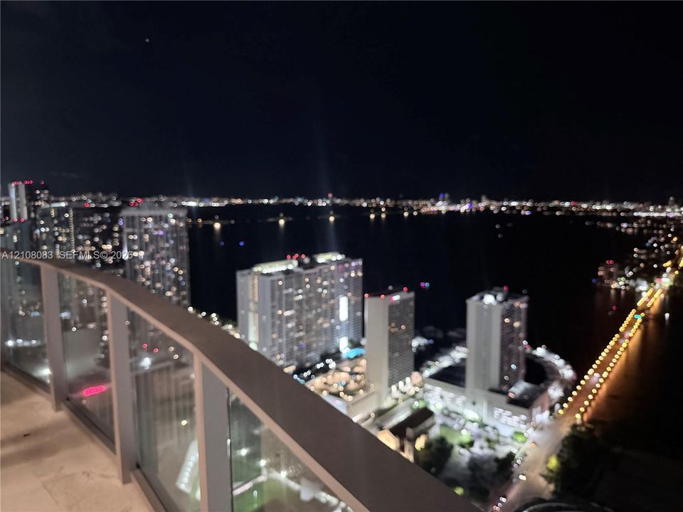 Covered balcony with a glass panel railing and panoramic water and cityscape scenery