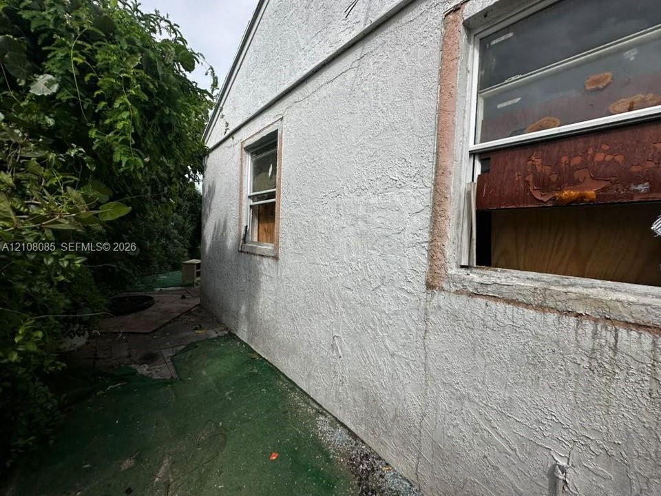 Stucco exterior featuring dual window openings and mature perimeter vegetation