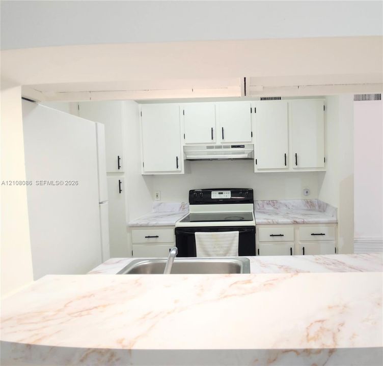 Kitchen featuring white cabinetry with dark hardware, stone-patterned countertops, a stainless steel sink, and a built-in range hood
