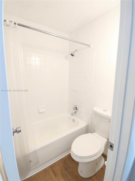 Bathroom featuring a porcelain tub, wall-mounted shower head, white ceramic tile surround, and wood-finish flooring