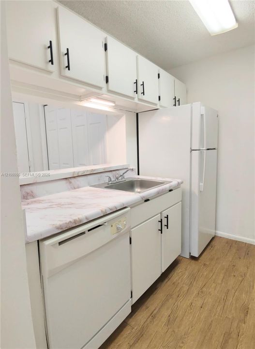 Kitchen featuring white cabinetry with matte black hardware, stone-pattern laminate countertops, stainless steel sink with a dual-handle faucet, and wood-finish flooring