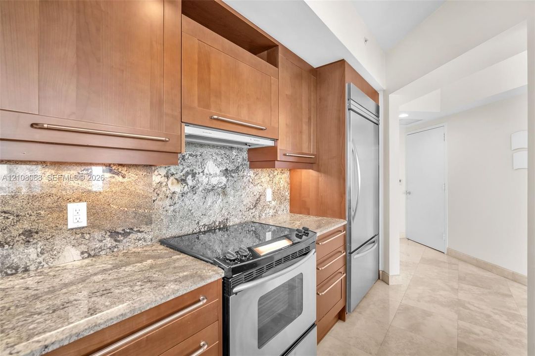 Kitchen featuring natural wood cabinetry, stone countertops, stone backsplash, stainless steel appliances, and stone flooring