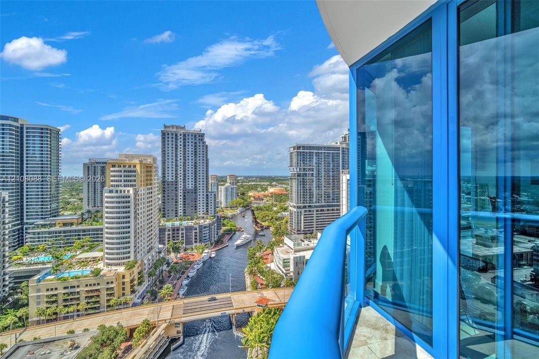 Actual view! Private balcony with blue glass railing featuring floor-to-ceiling blue-tinted windows and stone-tiled flooring