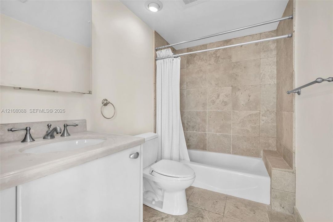 Bathroom featuring natural stone tile tub surround and flooring, vanity with stone countertop, recessed lighting, and metallic hardware