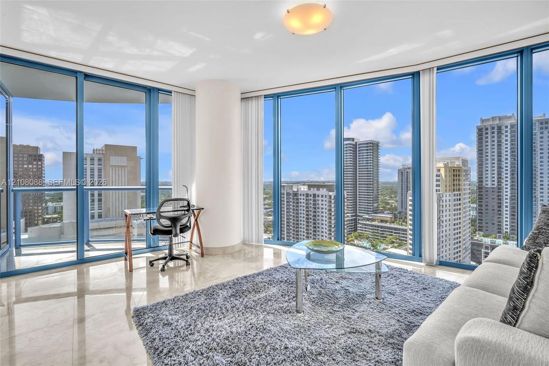 Guest Bedroom set up as a den or mdeia room. Floor-to-ceiling windows featuring panoramic urban scenery, polished stone flooring, and a glass balcony railing