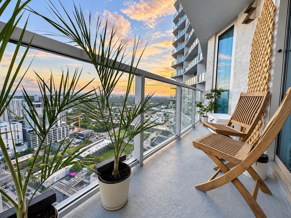 Covered balcony featuring glass railing, metal framework, and concrete flooring with sunset horizon backdrop