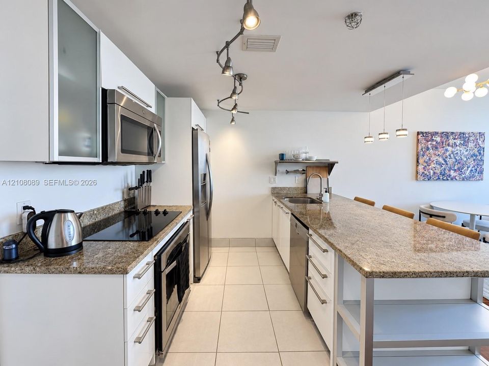Kitchen featuring white flat-panel cabinetry with frosted glass inserts, stone countertops, stainless steel appliances, tile flooring, and adjustable track lighting