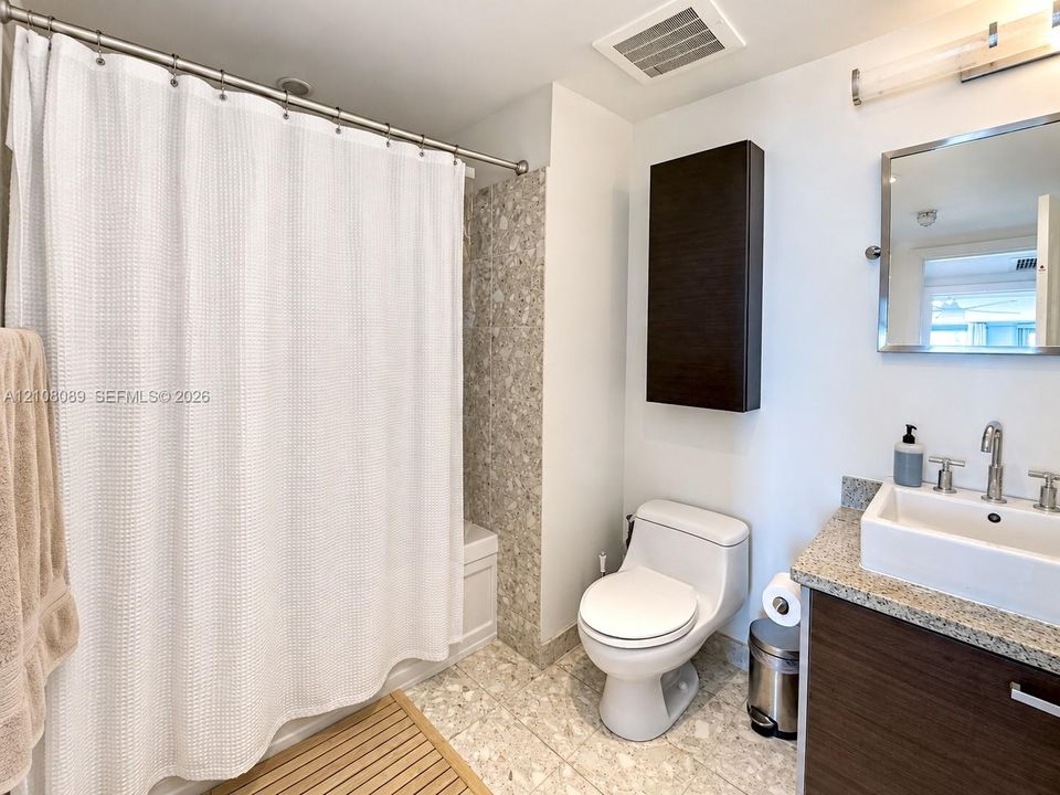 Bathroom featuring a vessel sink with a chrome faucet, stone-composite countertop, dark wood-finish cabinetry, wall-mounted storage cabinet, and mosaic tile surround