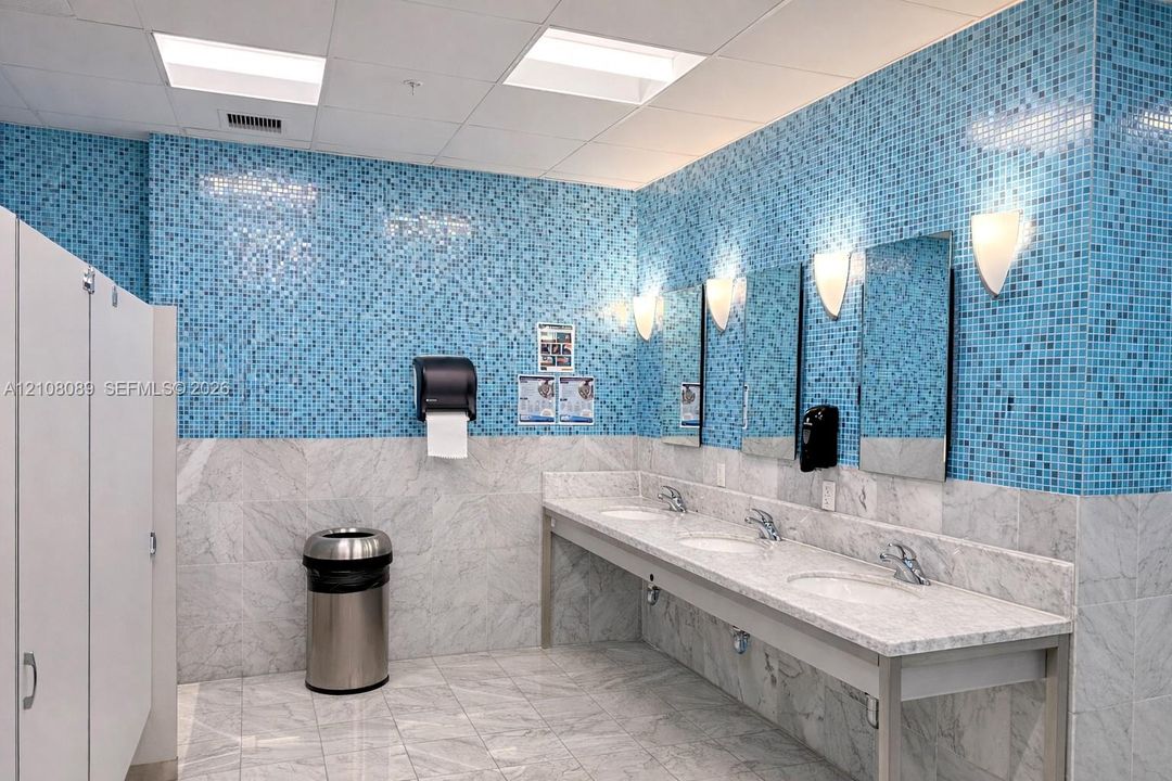 Multi-station stone vanity with integrated sinks, polished stone flooring, blue mosaic tile wall accents, and wall-mounted sconce lighting