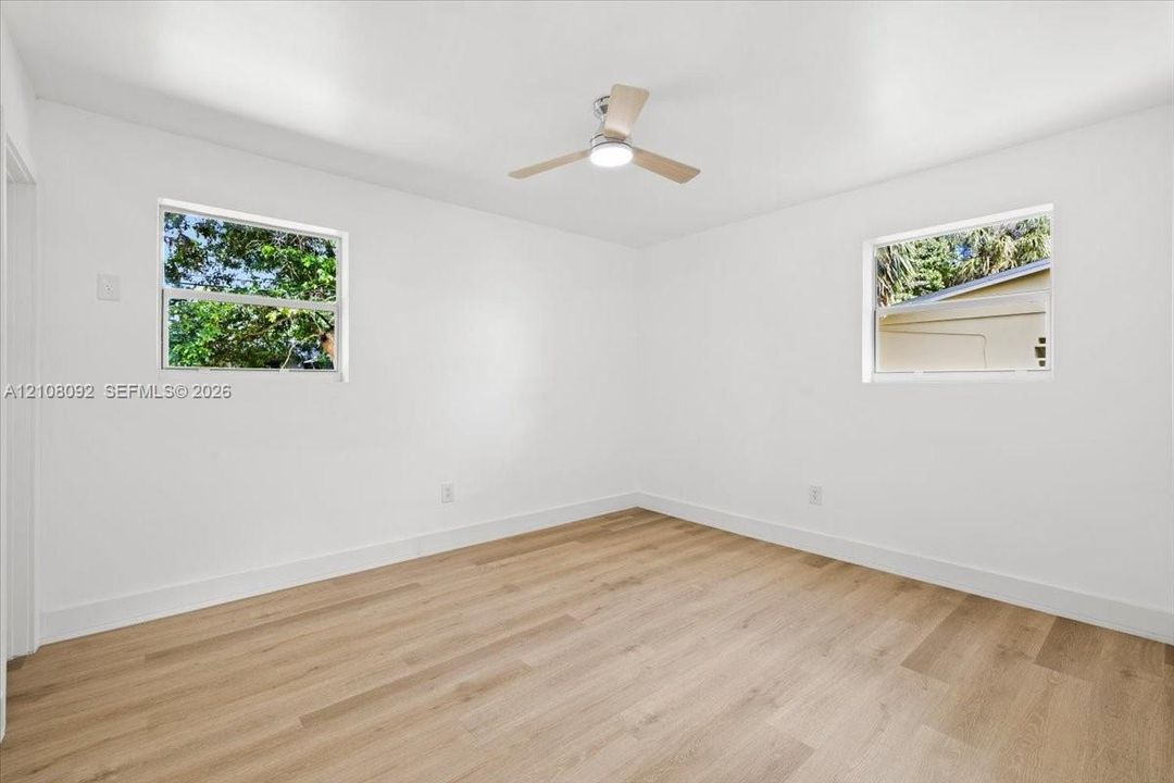 Bright room featuring wood-finish flooring, dual windows, and an integrated ceiling fan with light fixture