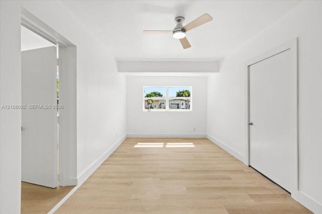 Interior space featuring wood-finish flooring, a neutral color palette, a central ceiling fan with integrated lighting, and a single-pane window