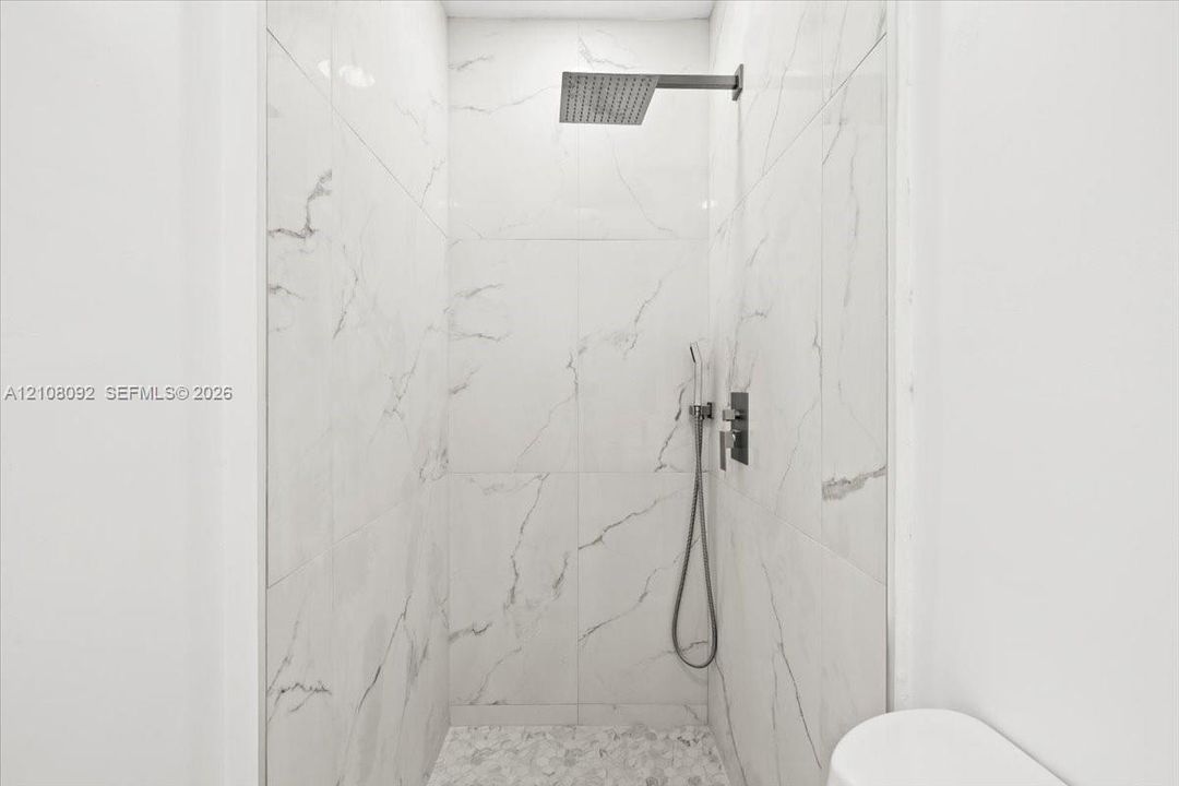 Walk-in shower featuring floor-to-ceiling large-format tile, wall-mounted rain shower head, handheld shower fixture, and stone-finish floor tile