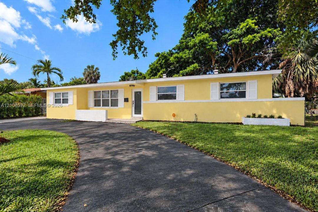 Single-story exterior featuring a stucco facade, curved asphalt driveway, built-in concrete planter, and window shutters