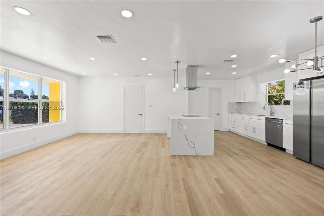 Kitchen featuring white shaker-style cabinetry, an island with a stone-finish countertop, stainless steel appliances, recessed lighting, and wood-finish flooring