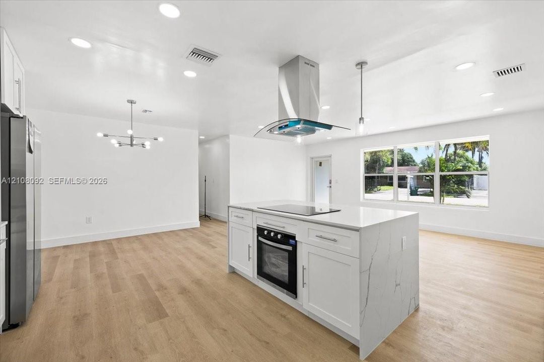 Kitchen featuring a central island with a stone-finish countertop and built-in electric cooktop, stainless steel chimney-style range hood, recessed ceiling lighting, and wood-finish flooring