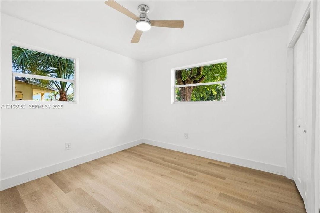 Interior space featuring wood-finish flooring, two dual-pane windows, a ceiling fan with integrated lighting, and a closet with bifold doors