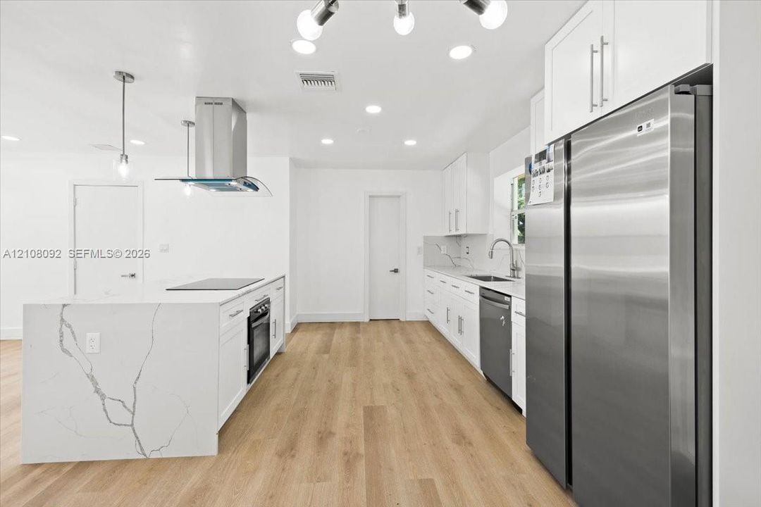 Kitchen featuring white cabinetry, wood-finish flooring, a waterfall-edge stone island with a built-in oven, stainless steel appliances, and a modern chandelier