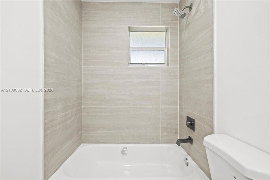 Bathtub with horizontal tile surround, square fixed-pane window, and matte black plumbing fixtures including a rainfall showerhead