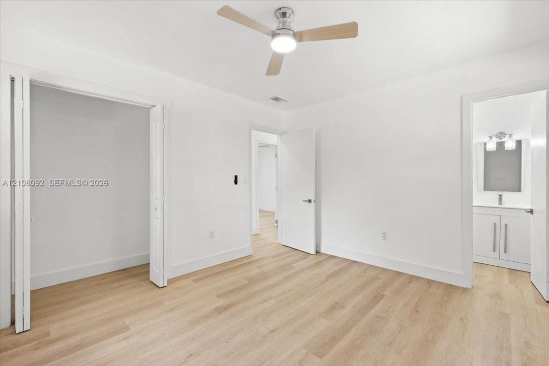 Neutral-toned interior featuring wood-finish flooring, a contemporary three-blade ceiling fan with integrated lighting, bi-fold closet doors, and solid-core interior doors