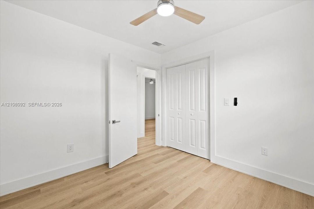 Room featuring wood-finish flooring, white walls, double-door closet, and an integrated ceiling fan with light fixture