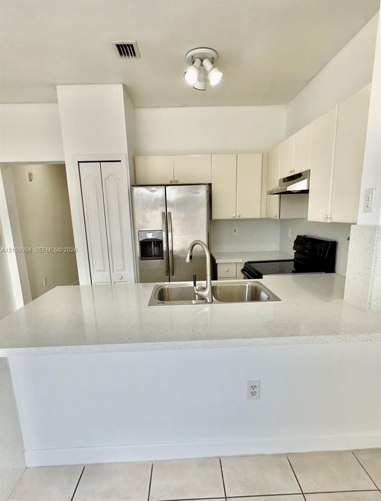 Kitchen featuring a stone-composite countertop, dual-basin stainless steel sink with a high-arch faucet, stainless steel side-by-side refrigerator, flat-panel cabinetry, and tile flooring