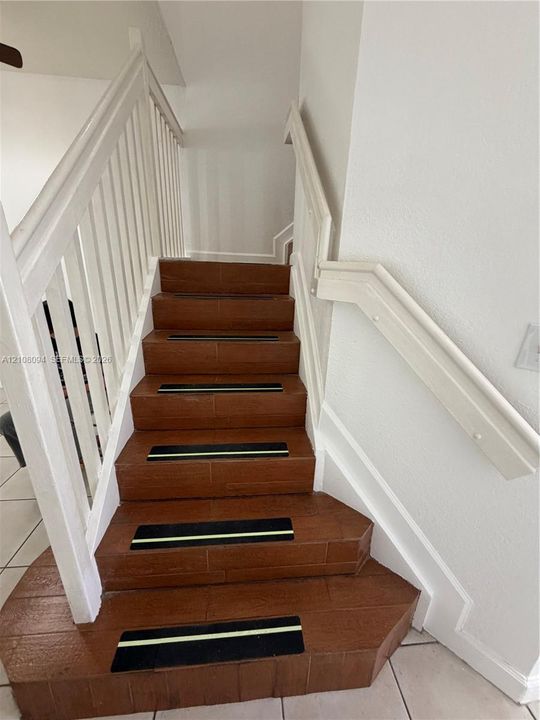 Staircase featuring wood-finish treads, white painted railing, and integrated non-slip step strips