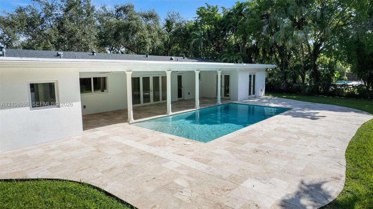 Rear exterior featuring a covered patio with columns, a rectangular swimming pool, and stone paver decking