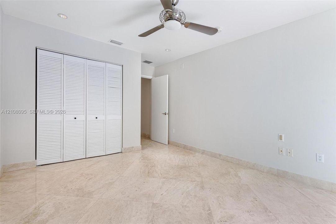 Neutral stone flooring, louvered closet doors, recessed ceiling lighting, and a brushed-metal ceiling fan